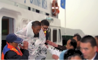 被解救上来的落海船员李良友正被救援人员抬上岸.